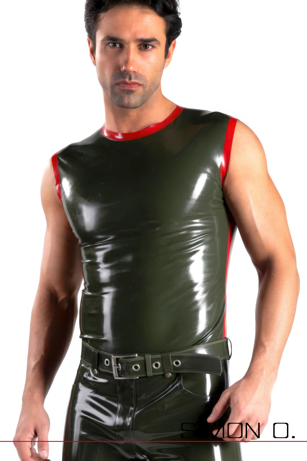 Ein Mann trägt ein glänzendes dunkelgrünes Latex-Tanktop mit rotem Besatz und einem schwarzen Gürtel und steht selbstbewusst vor einem schlichten dunklen Hintergrund.