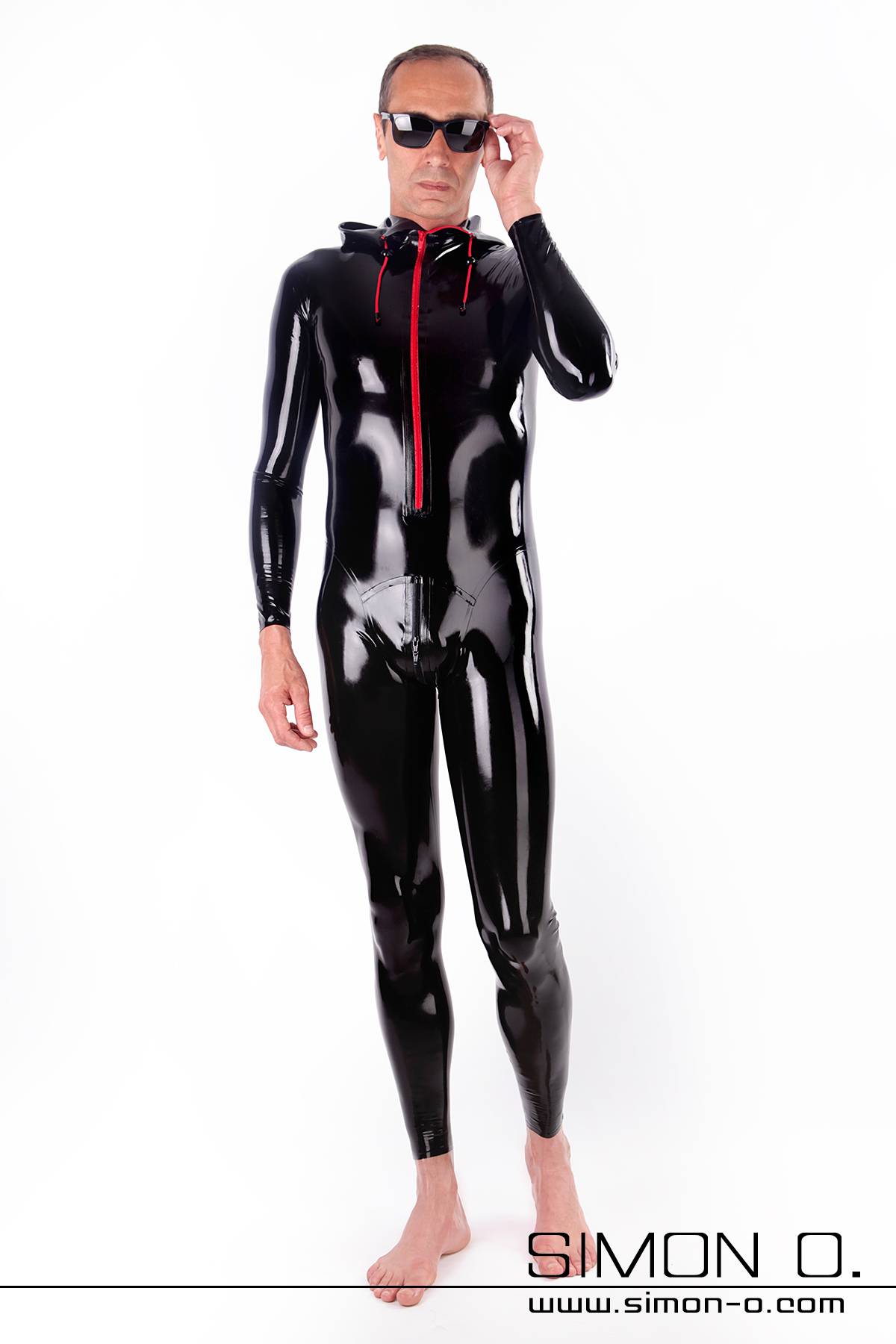 Herren Latex Catsuit zipp vorne Eine Mann mit dunkler Sonnenbrille in einem glänzenden schwarzen Latex-Catsuit mit rotem Reißverschluss vorne.