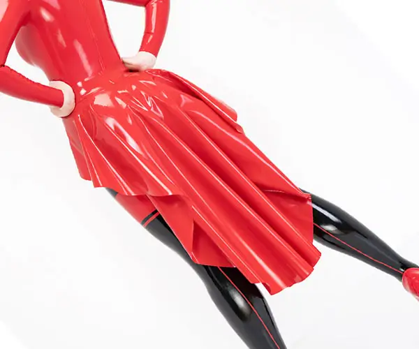 Eine Frau, die einen glänzenden roten Tellerrock und ein Oberteil aus Latex mit schwarzen Strümpfen trägt, die Hände auf den Hüften, vor einem schlichten weißen Hintergrund.