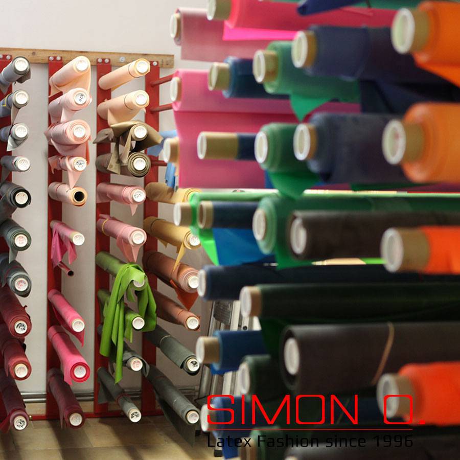 Latex material on rolls Rolls of latex material in pink, green and beige and many other colours are stacked on wall shelves. The text reads: "SIMON O. Latex fashion since 1996.".