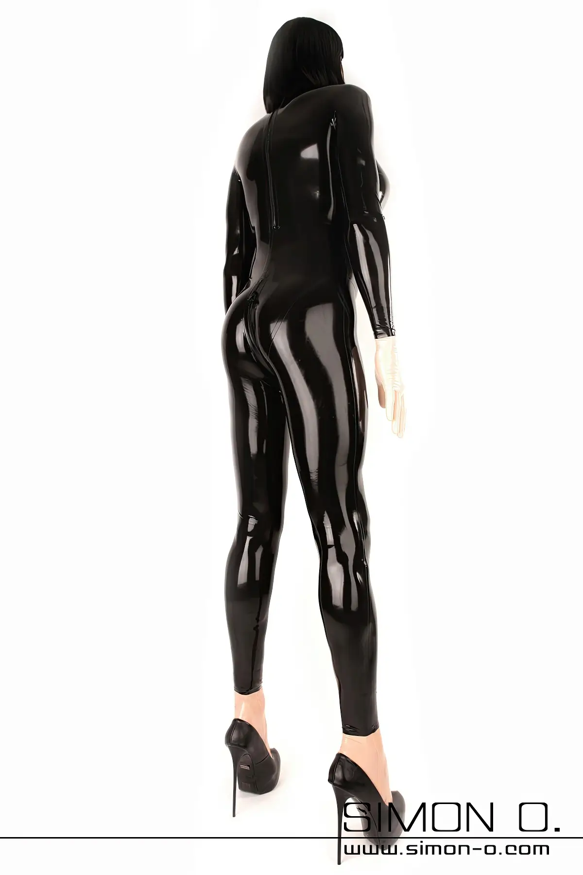 A man wears a black rubber doll suit with breasts and high heels