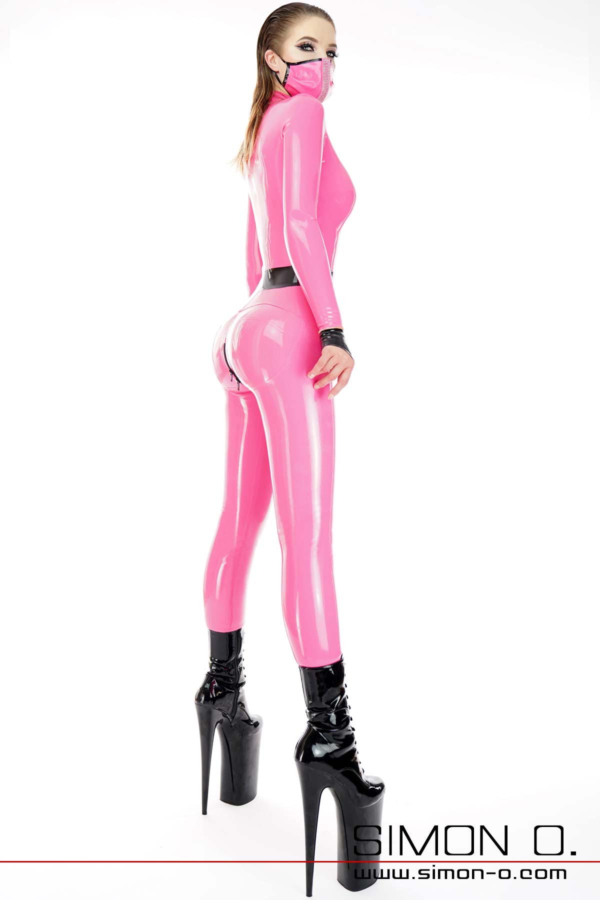 Latex Catsuit mit Push Up Gesäß Bereich Ein schlankes Model trägt einen Latex Catsuit mit Push Up Gesäß Bereich. Der Latex Catsuit hat die Farbe Pink mit schwarz kombiniert.