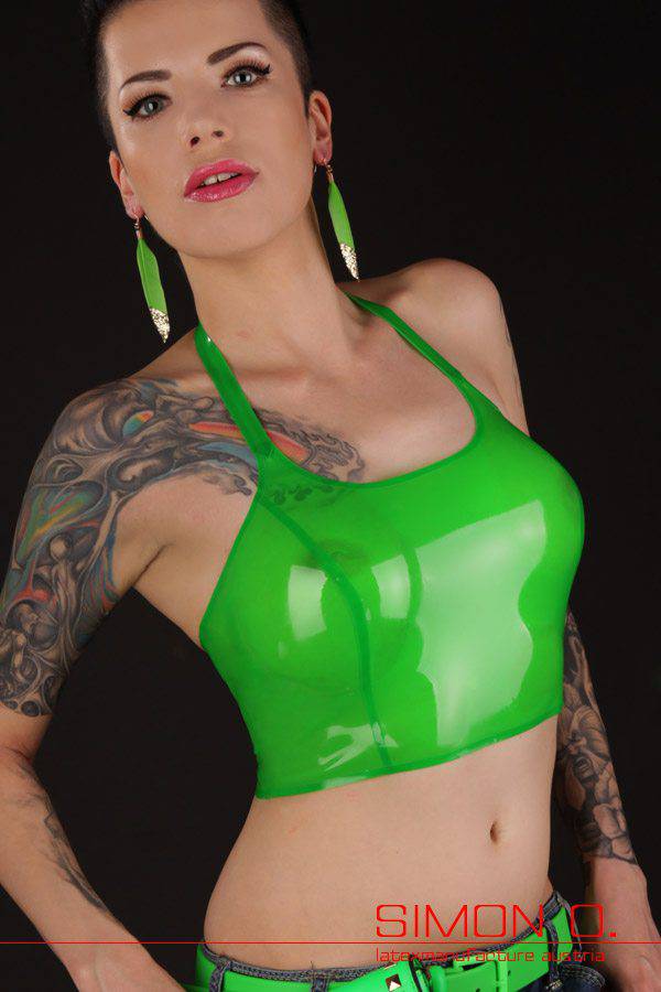 neckholder latex top Eine Frau mit großen Ohrringen und Tattoos posiert in einem glänzenden, hellgrünen Neckholder-Latex-Top vor einem dunklen Hintergrund.