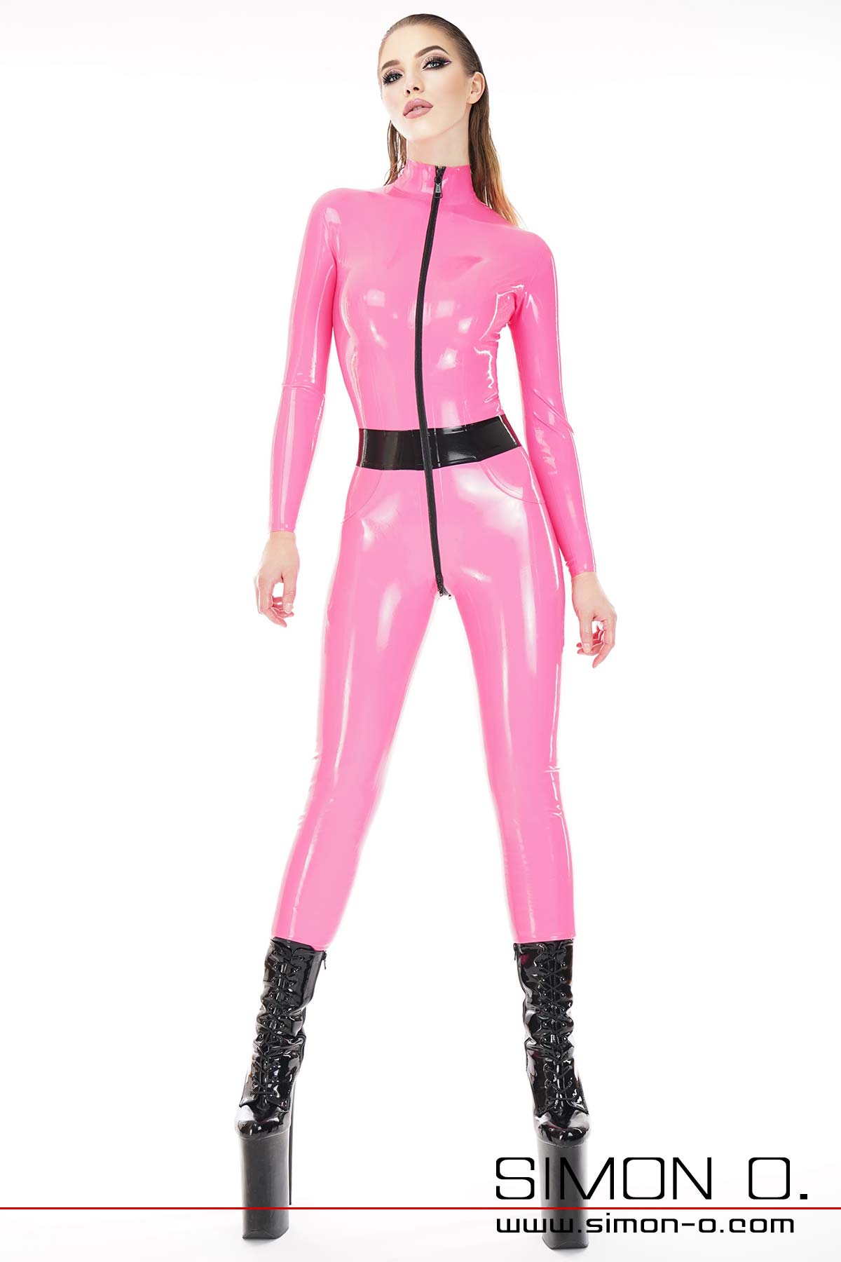 Pink Latex Catsuit mit schwarz kombiniert. Ein Model trägt einen hautengen pink farbigen Latex Catsuit mit schwarzen Zipp und Gürtel. Dazu trägt Sie schwarze Platform High Heels.