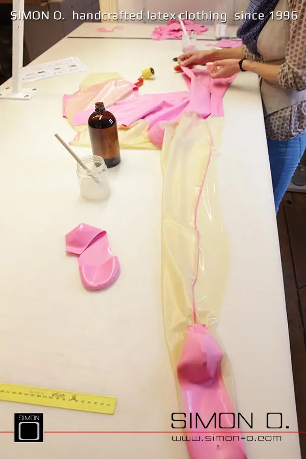 La production d'un catsuit en latex rose avec une partie transparente pour les jambes est montrée, en commençant par le découpage et le collage jusqu'au produit fini.