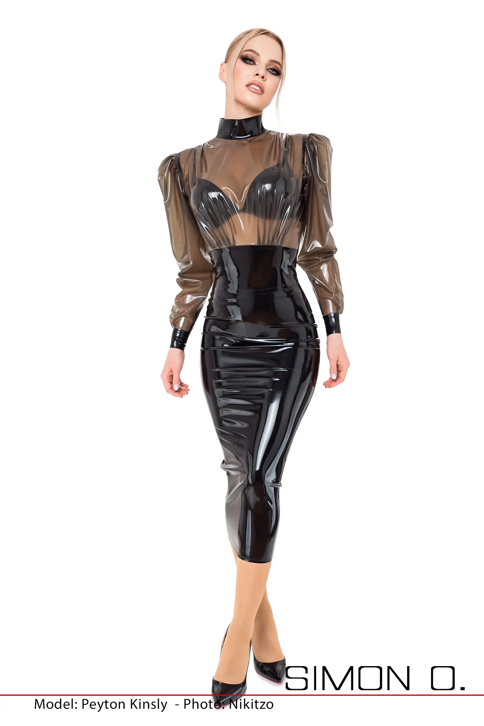 A woman poses in a black transparent latex blouse combined with a fitted, black latex pencil skirt and high heels.