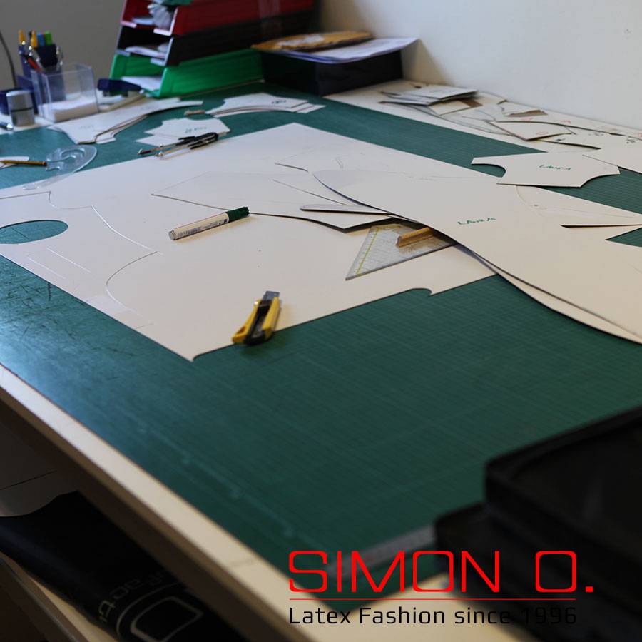 Workplace latex pattern A work area with cutting pieces, rulers, cutters and pens on a green cutting mat. The text "SIMON O. Latex Fashion since 1996" is visible.