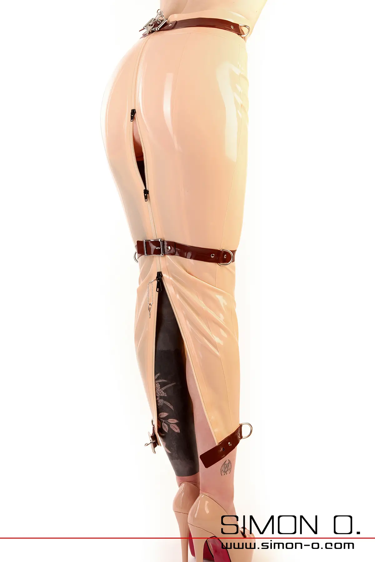 Person in skin tone latex skirt with brown ankle straps and zip at the back, standing seen from behind.