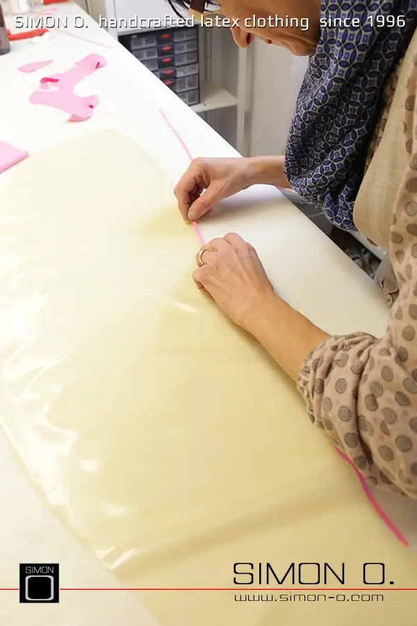 La production d'un catsuit en latex rose avec une partie transparente pour les jambes est montrée, en commençant par le découpage et le collage jusqu'au produit fini.