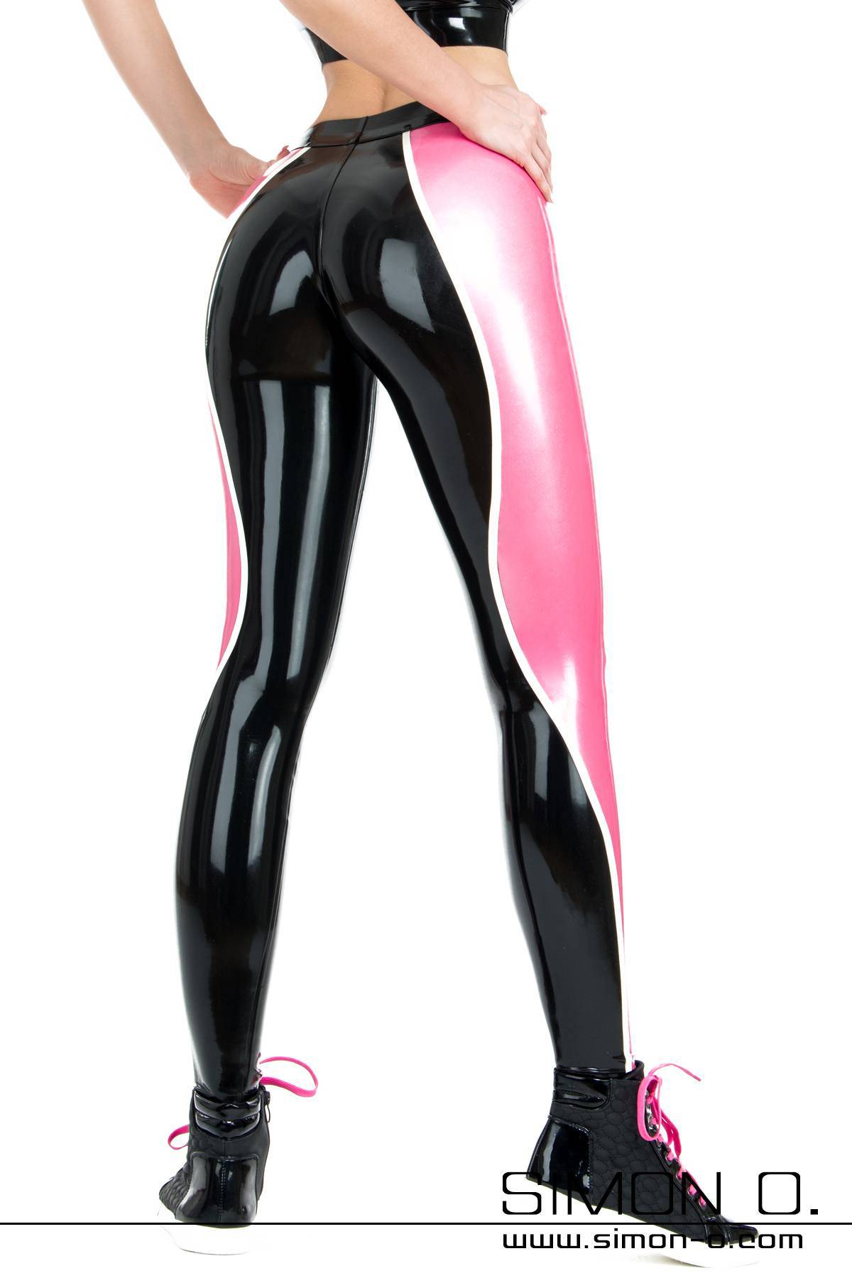 Latex leggings 3 coloured One person stands with their face turned away, presenting latex leggings in shiny black and pink with matching trainers, their hands resting confidently on their waist.