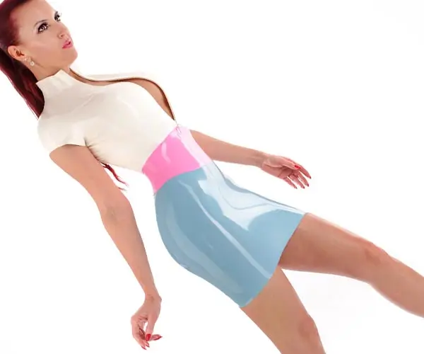 Eine Person mit langen roten Haaren trägt ein glänzendes, körperbetontes Latexkleid in Weiß, Rosa und Blau. Das Kleid ist hochglänzend und liegt hauteng an.
