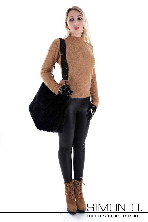 Eine Frau mit Pullover Vor einem weißen Hintergrund steht eine Frau, die einen hellbraunen Pullover, schwarze Leggings, braune Stiefel und schwarze Handschuhe trägt und eine große schwarze Umhängetasche trägt.
