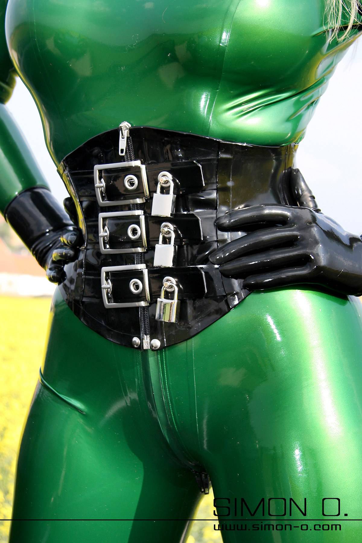 Latex corset with lock lockable in black A person in a shiny green latex catsuit and black gloves wears a black latex corset with locks.