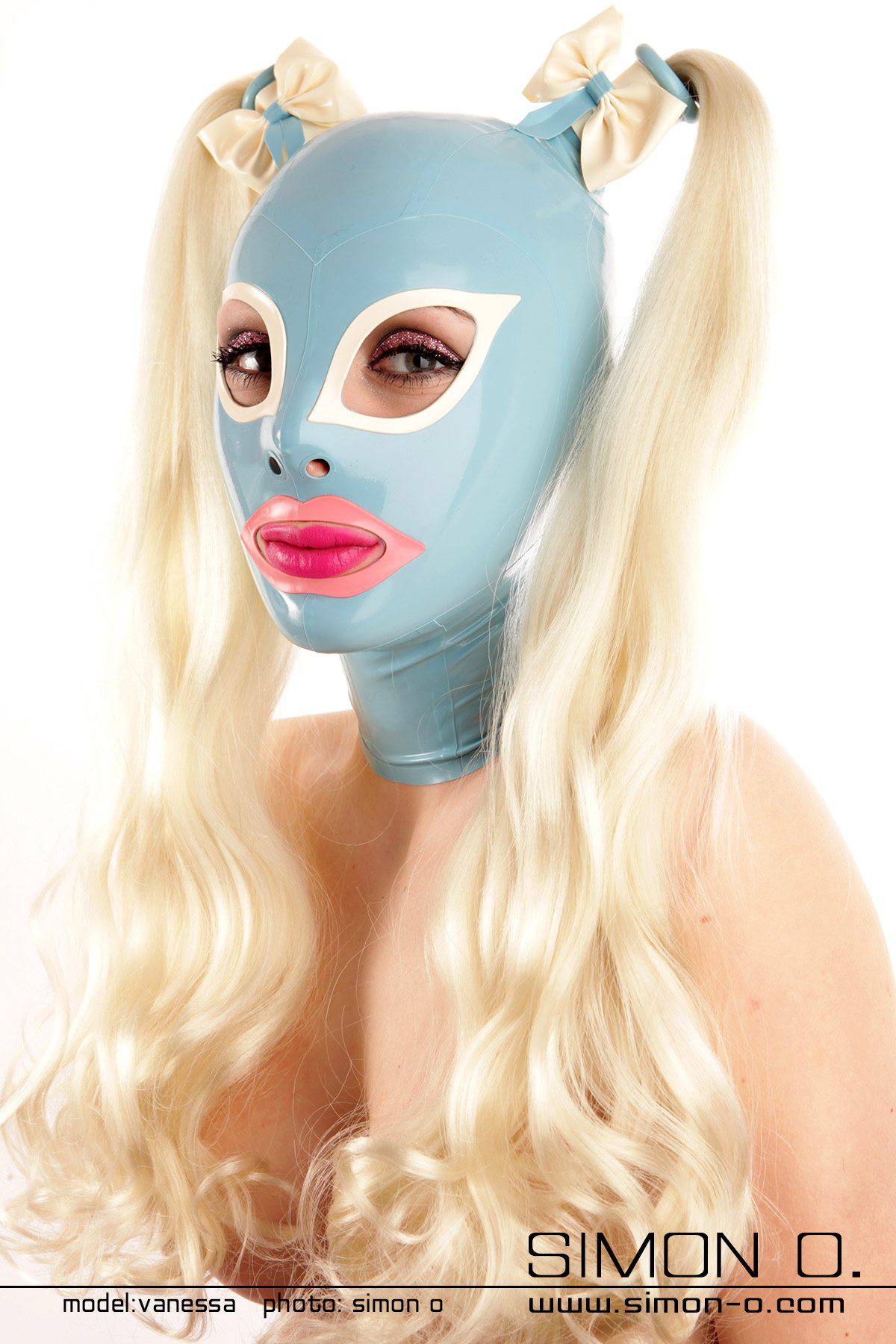 Latexmaske mit weißen Augenausschnitten Eine Person trägt eine hellblaue Latexmaske mit weißen Augenausschnitten und rosa Lippen, geschmückt mit weißen Schleifen und langen blonden Pferdeschwänzen.