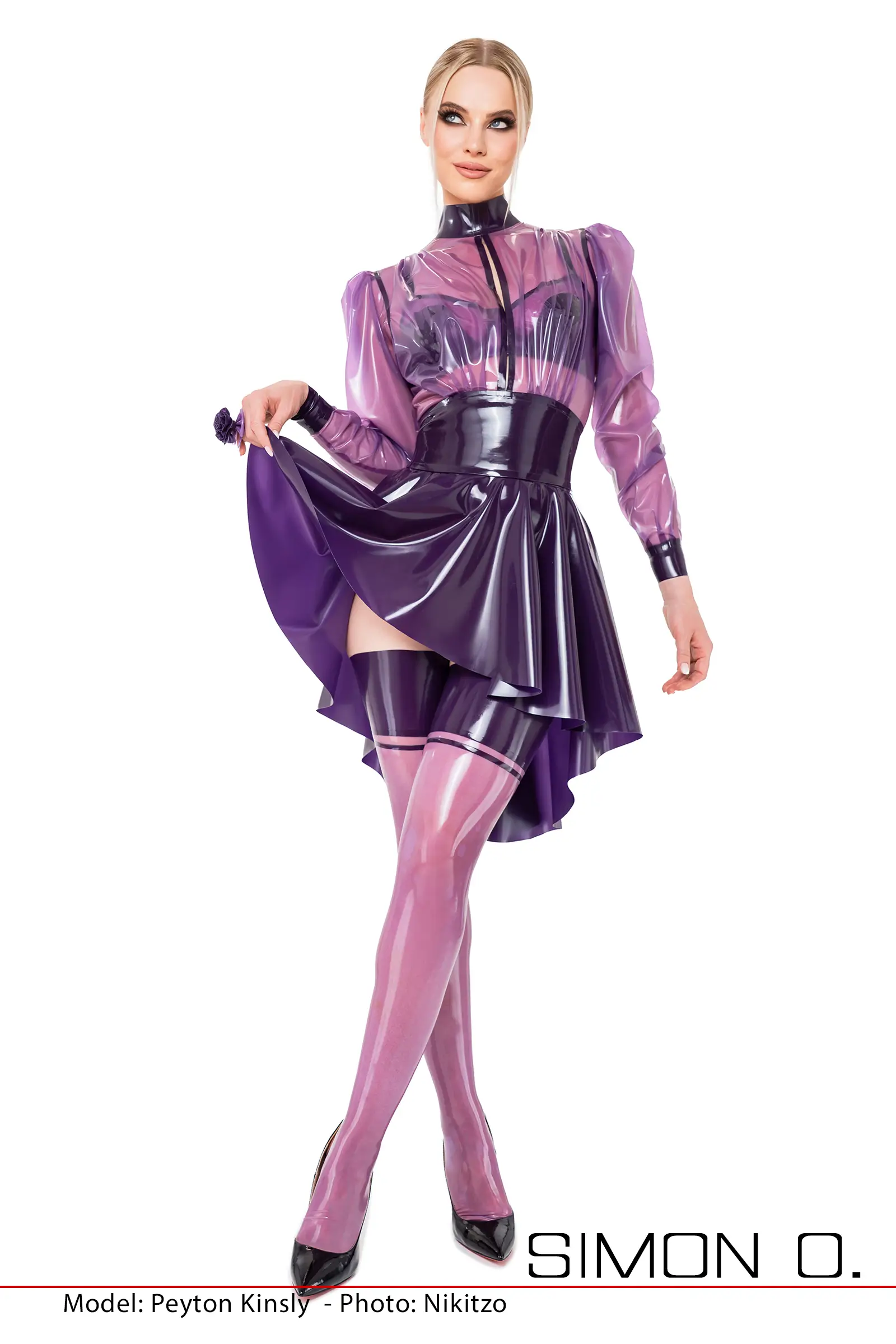 A woman poses in a purple transparent latex blouse with an opening in the chest area, wearing matching latex stockings and a swinging latex circle skirt.