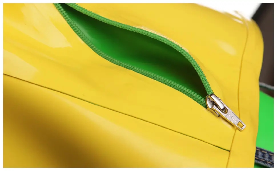 Nahaufnahme einer gelben Tasche, die Details der Latexverarbeitung zeigt, mit einem teilweise geöffneten grünen Reißverschluss, der ein grünes Inneres offenbart.