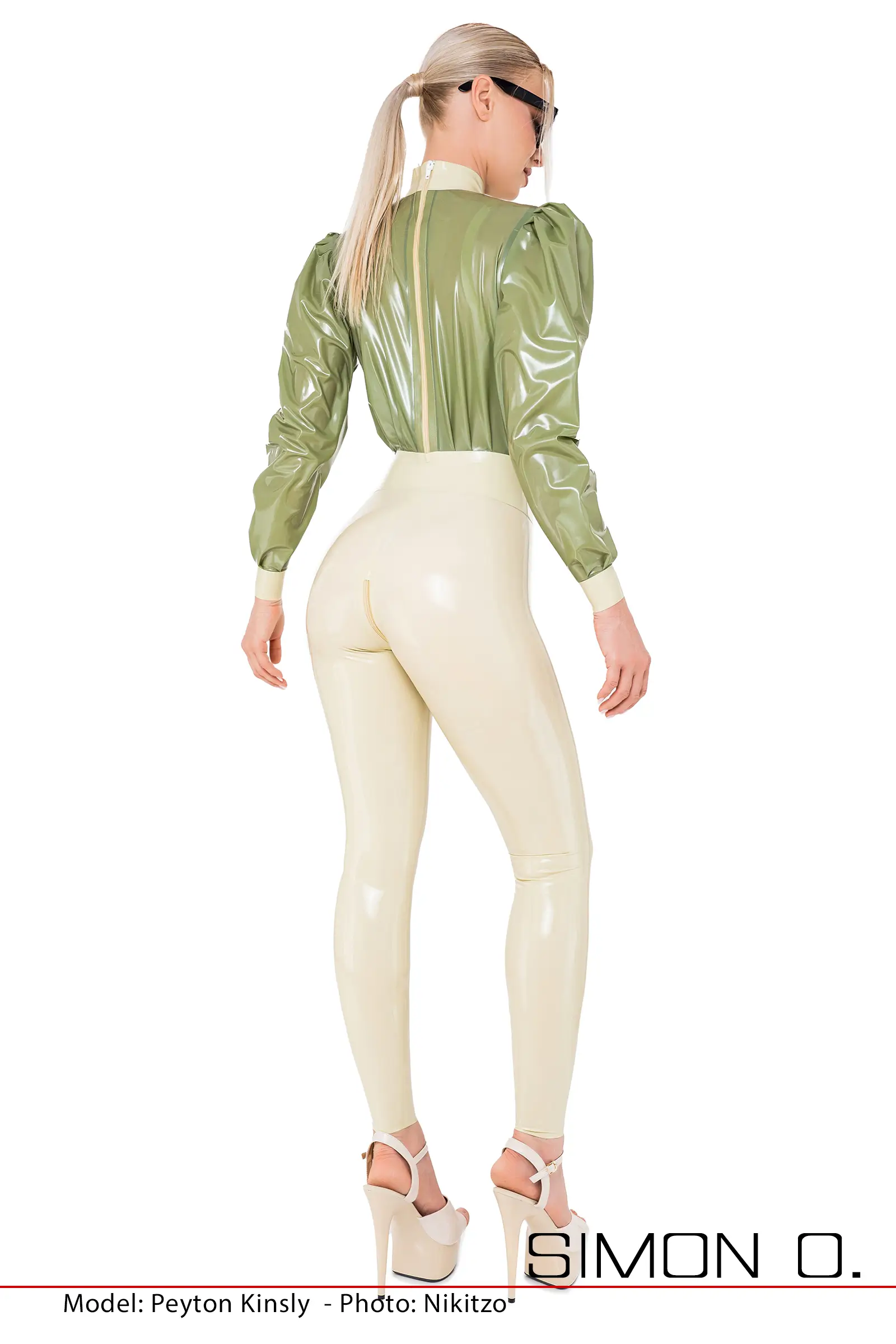 Eine Frau trägt einem beigen Latex Catsuit mit lockeren Oberteil in grün welcher einen Zipp auf der Rückseite hat, von hinten gesehen.