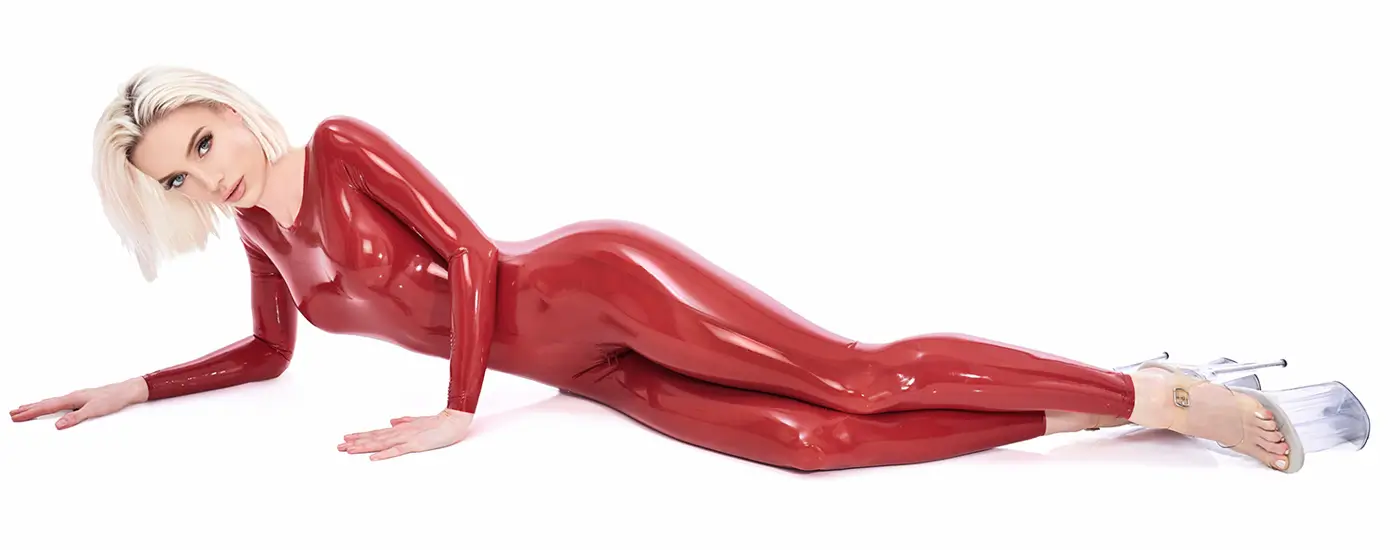 Tight wetlook latex catsuit red A woman with short blonde hair lies on her side wearing a shiny red wetlook latex catsuit and transparent high heels against a white background.