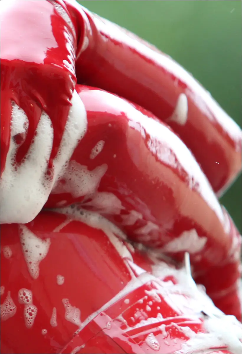 Detailfoto eines nassen roten Latex Outfit welches mit Schaum gewaschen wird