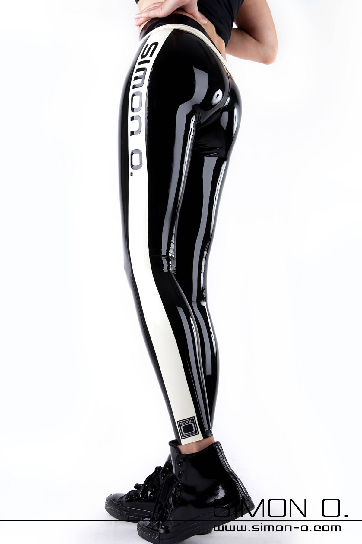 Sporty glossy latex leggings in black One person wears black latex leggings with a white "Simon O." side stripe and black high-top sneakers and stands in front of a white background.