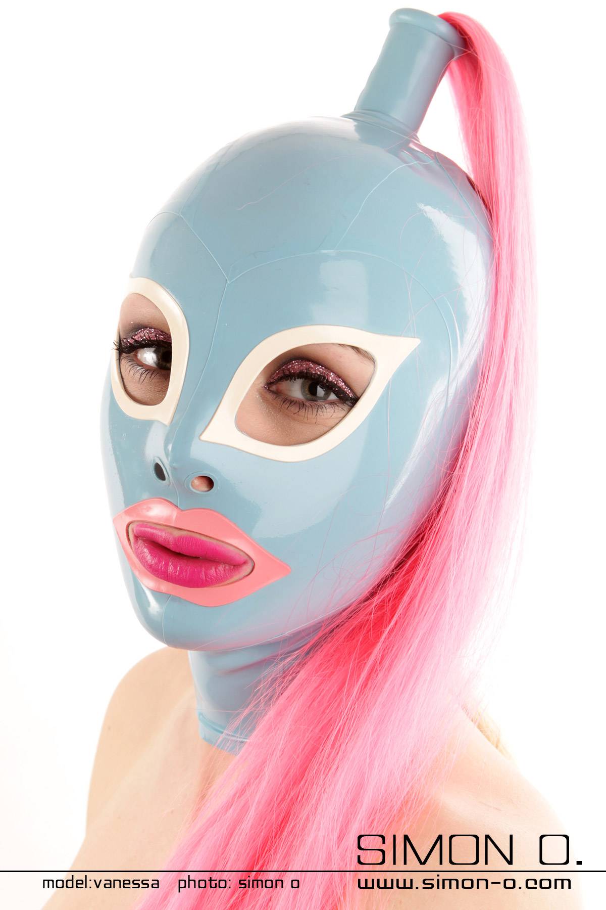 Latex Maske mit Katzenaugen in hellbalu Eine Frau trägt eine glänzend blaue Latexmaske mit weißen Katzenaugen und rosa umrandeten Mund. Ergänzt wird die Maske durch einen langen rosa Pferdeschwanz.