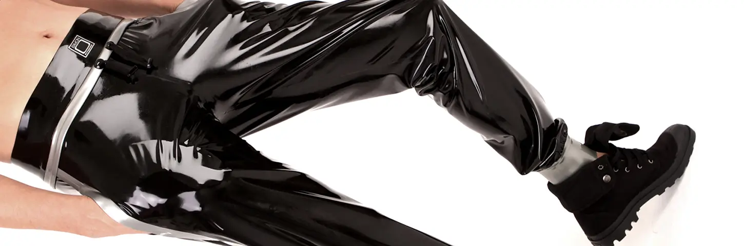Herren Latex Joggingshose Ein Mann trägt eine glänzende schwarze Latex-Jogginghose und hat die Hände in der Tasche.