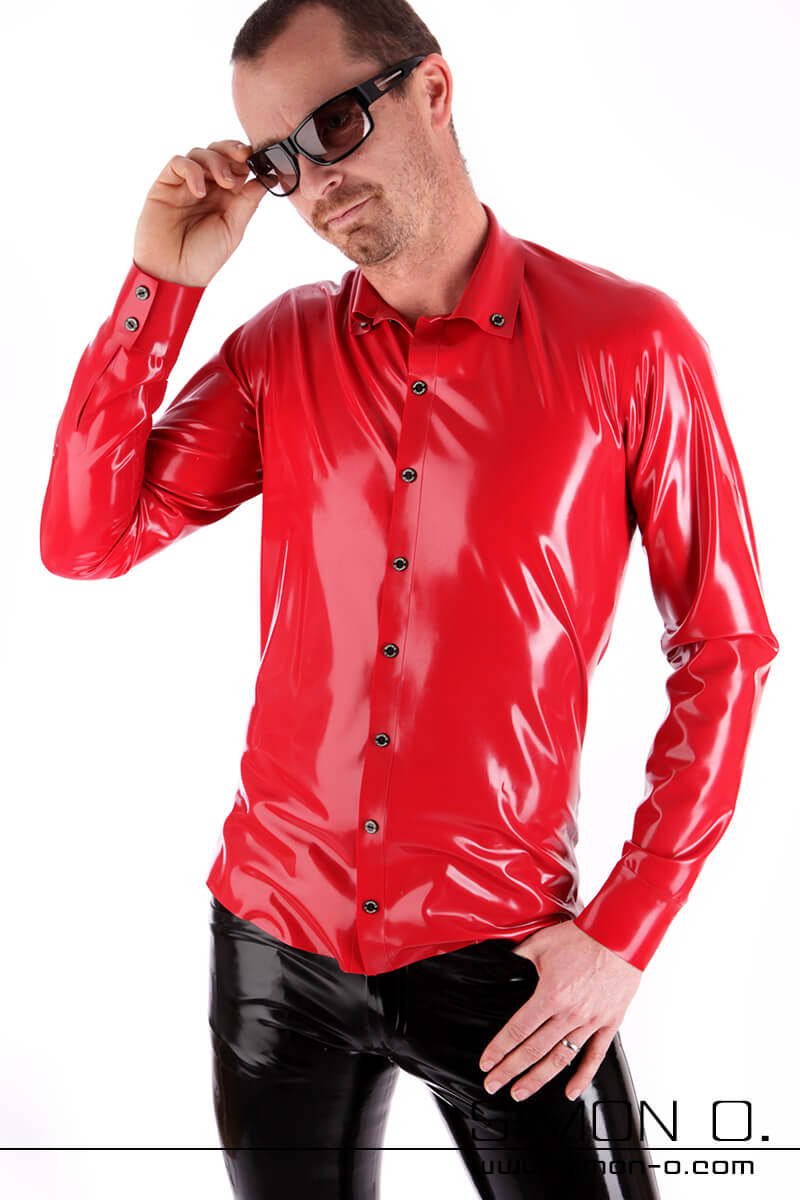 Latex Hemd für Herren in rot Ein Mann mit dunkler Sonnenbrille, einem glänzenden roten Latexhemd und einer glänzenden schwarzen Hose steht vor einem weißen Hintergrund und hat eine Hand auf der Hüfte.