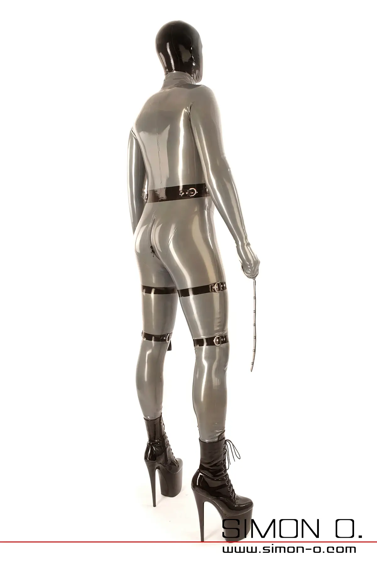 Person in a full-body latex bondage suit with mask, high-heeled boots, thigh straps and mittens with ankle straps seen from behind.