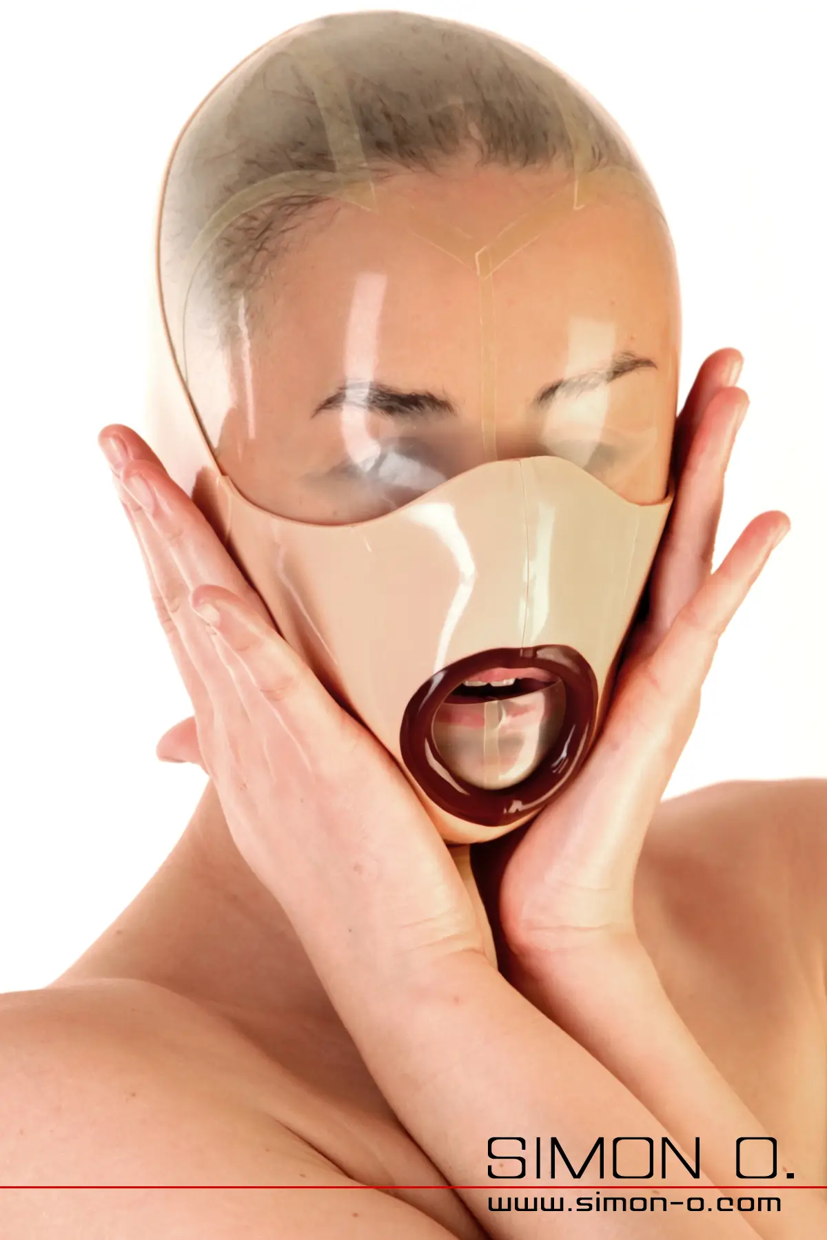 Eine Person, die eine durchsichtige, hautenge Blowjob-Latexmaske mit einer runden Mundöffnung trägt; die Hände sind auf das Gesicht gelegt.