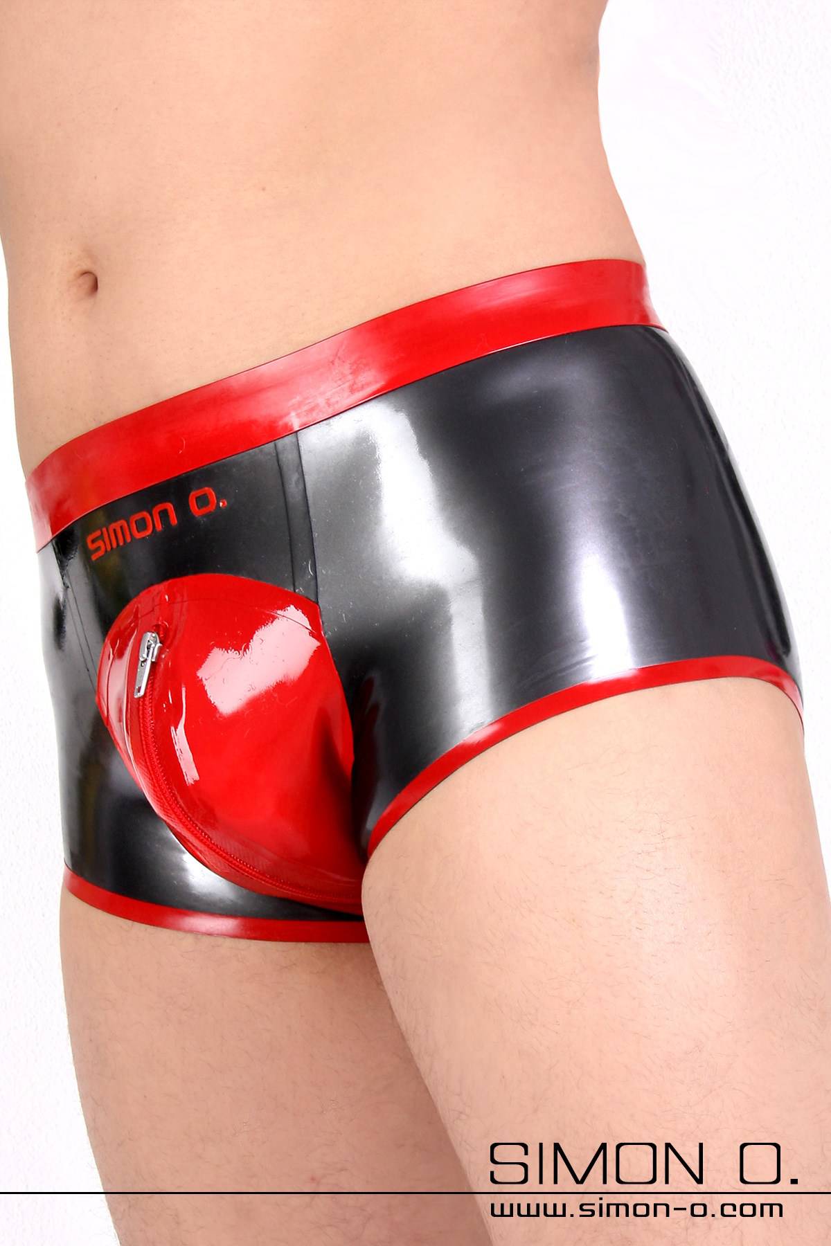 A man wears a shiny men's latex shorts with zipper in the crotch area, in the color metallic grey combined with red.