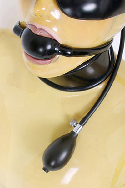 Eine Frau mit transparenter Latex Maske hat einen schwarzen Knebel im Mund und trägt eine Augenbinde aus Latex