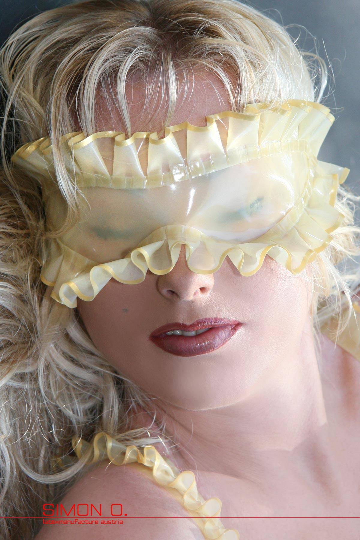 A blonde lady with red lips wears a latex blindfold