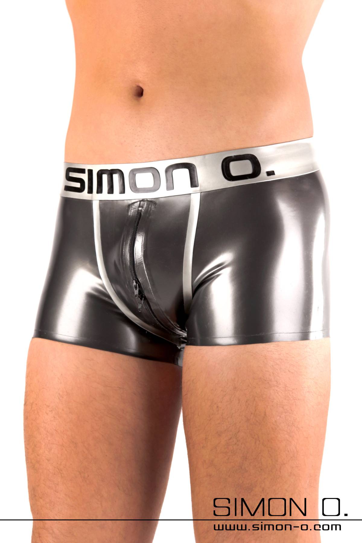 A man wears skintight shiny latex shorts with a Simon O. Logo on the waistband